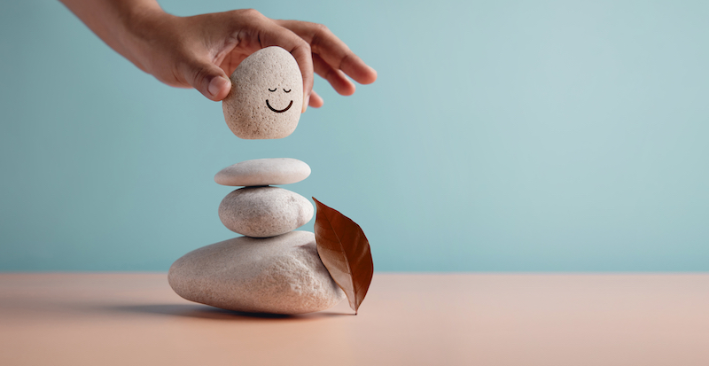 Enjoying Life Concept. Harmony and Positive Mind. Hand Setting Natural Pebble Stone with Smiling Face Cartoon to Balance. Balancing Body, Mind, Soul and Spirit. Mental Health Practice