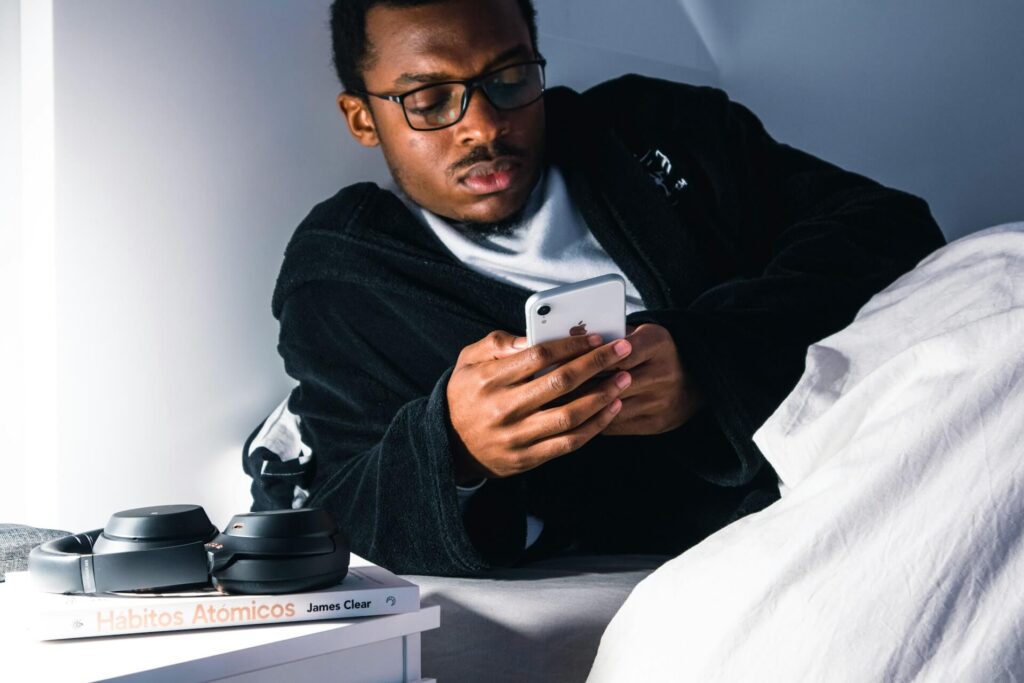 Person lying in bed holding a smartphone, illustrating doomscrolling behavior at night and its relationship to increased stress and exacerbation of tinnitus symptoms.