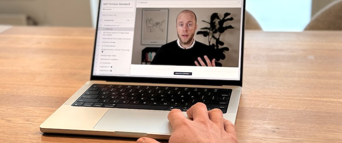 Laptop­scherm met een videoles uit de online cursus Sus Tinnitus, met Roel van Gorkum als presentator, die de inhoud uitlegt en het gestructureerde, videoge­baseerde onderdeel van het zelf­gestuurde, evidence­based tinnitus­behandel­programma illustreert.