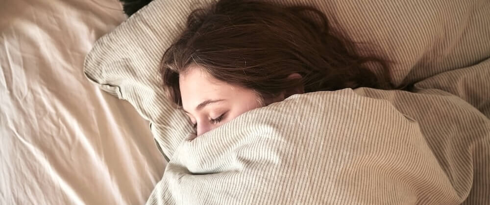 Persoon die met gesloten ogen in bed ligt, ter illustratie van slaapproblemen die vaak samengaan met tinnitus en het belang van op slaap gerichte behandelstrategieën bij tinnitusbehandeling.