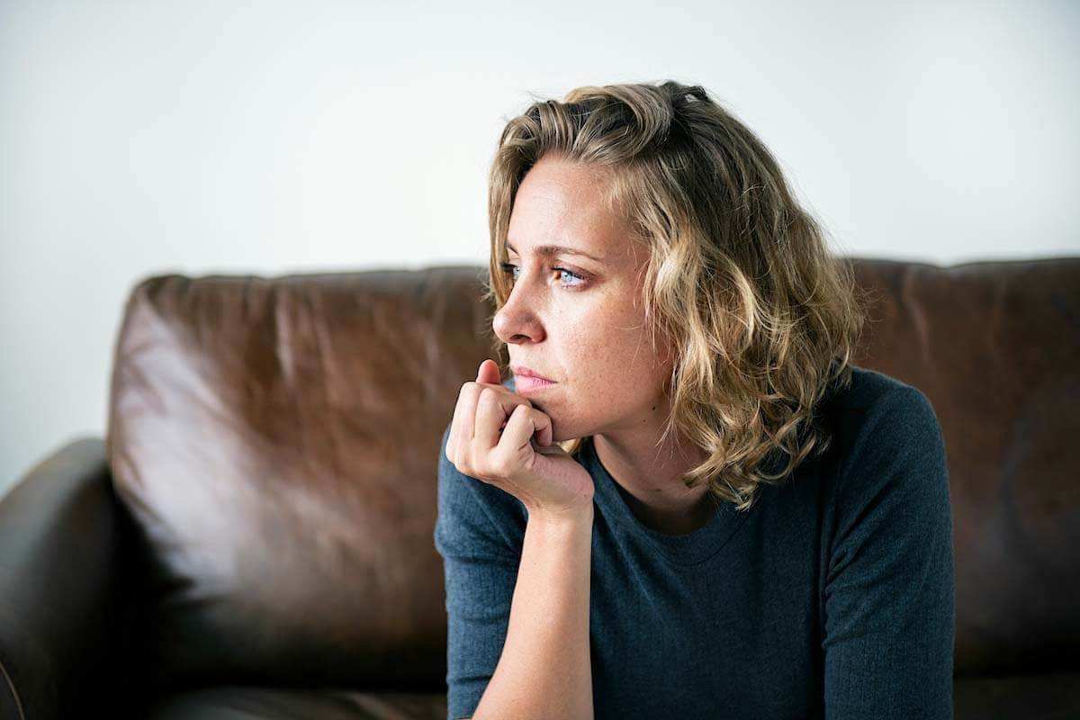 Woman sitting on a couch looking to her left with a thoughtful expression, used to illustrate the emotional or daily life impact of tinnitus.