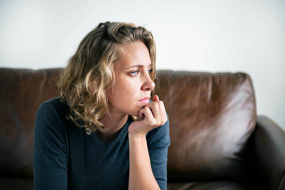 Woman sitting on a couch looking to her right with a thoughtful expression, used to illustrate the emotional or daily life impact of tinnitus.